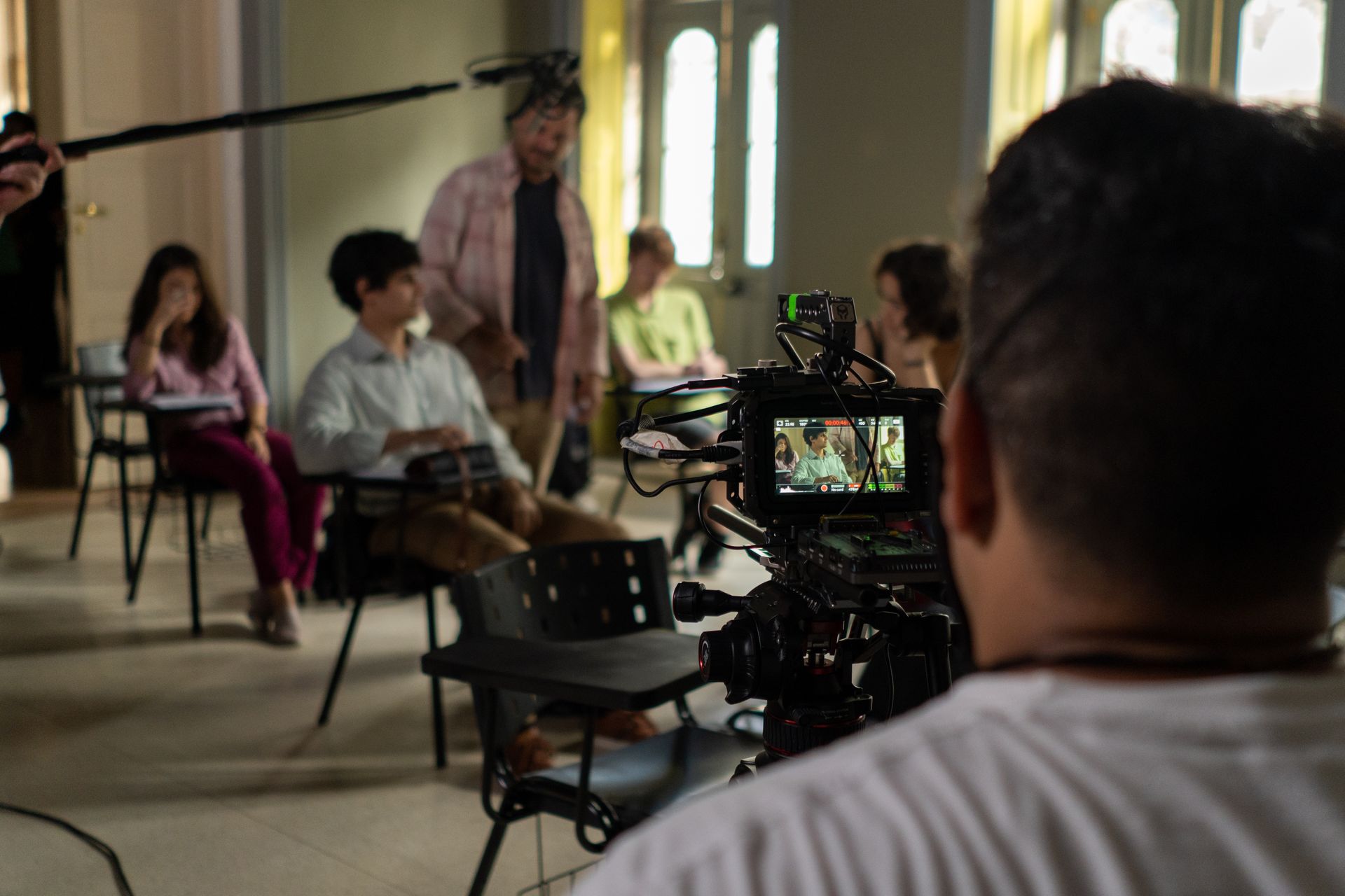 A man is looking at a camera while a group of people sit in chairs.