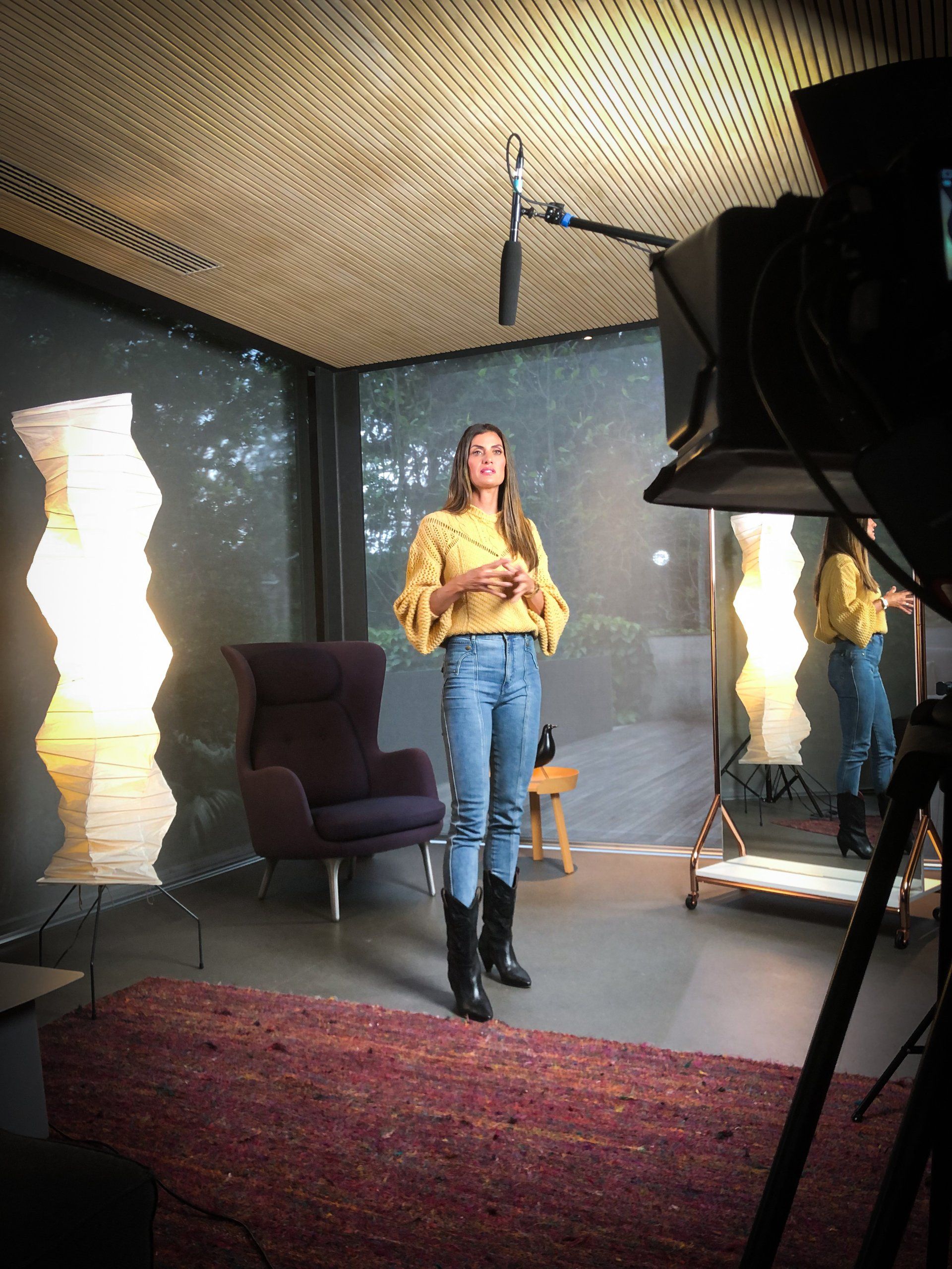 Uma mulher está diante de uma câmera em uma sala.