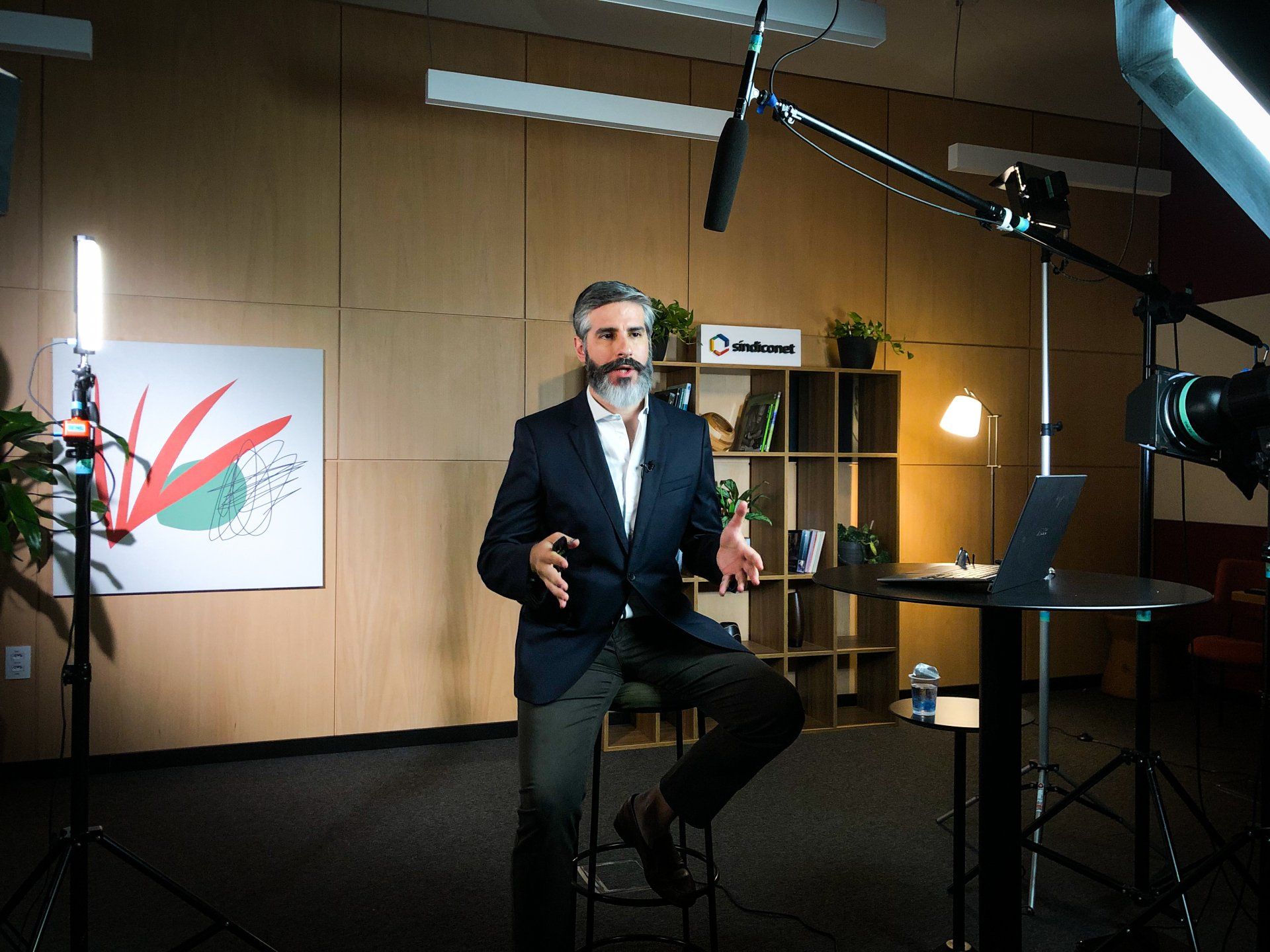 Um homem de terno está sentado em frente a um microfone em uma sala.