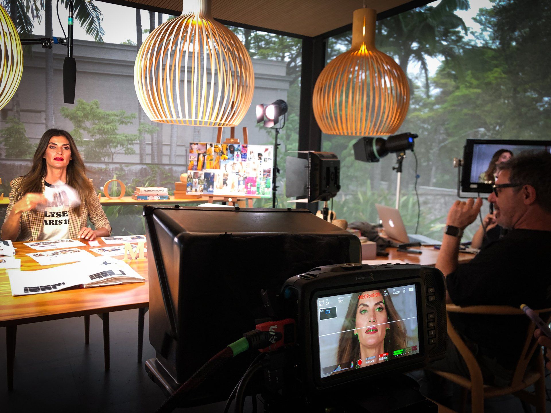 Mulher sentada à mesa com papéis. Duas luminárias pendentes estão penduradas acima dela.