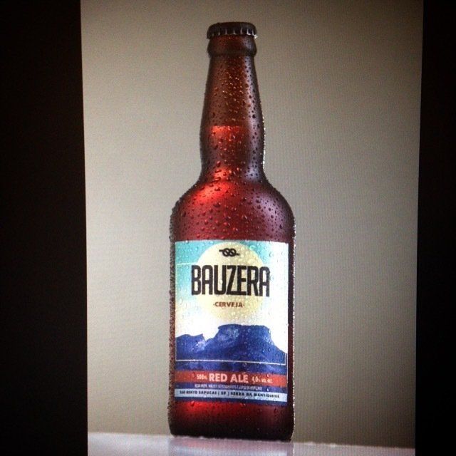 Uma garrafa de cerveja vermelha bauza está sobre uma mesa