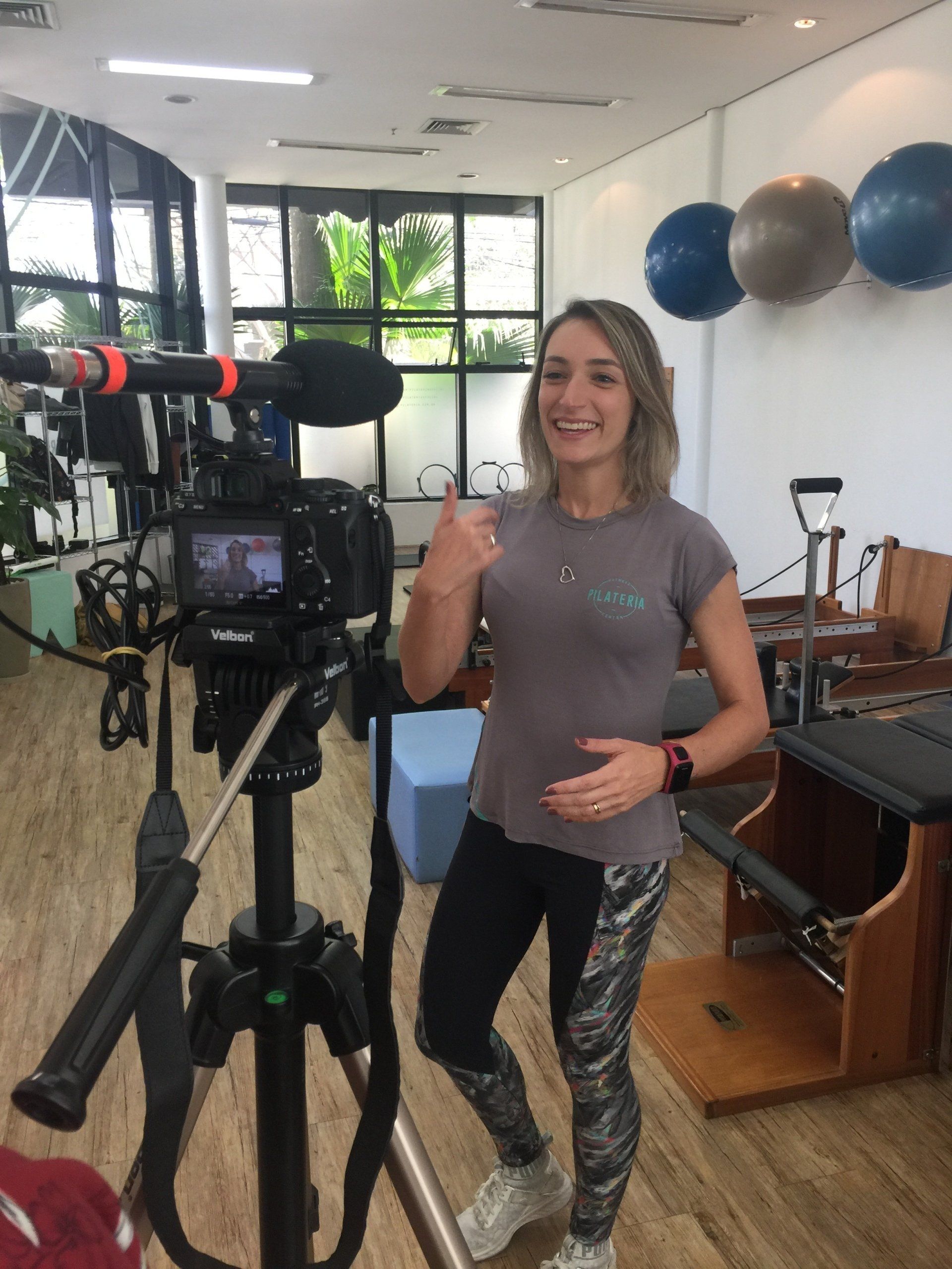 Uma mulher está diante de uma câmera em uma academia fazendo sinal de positivo.