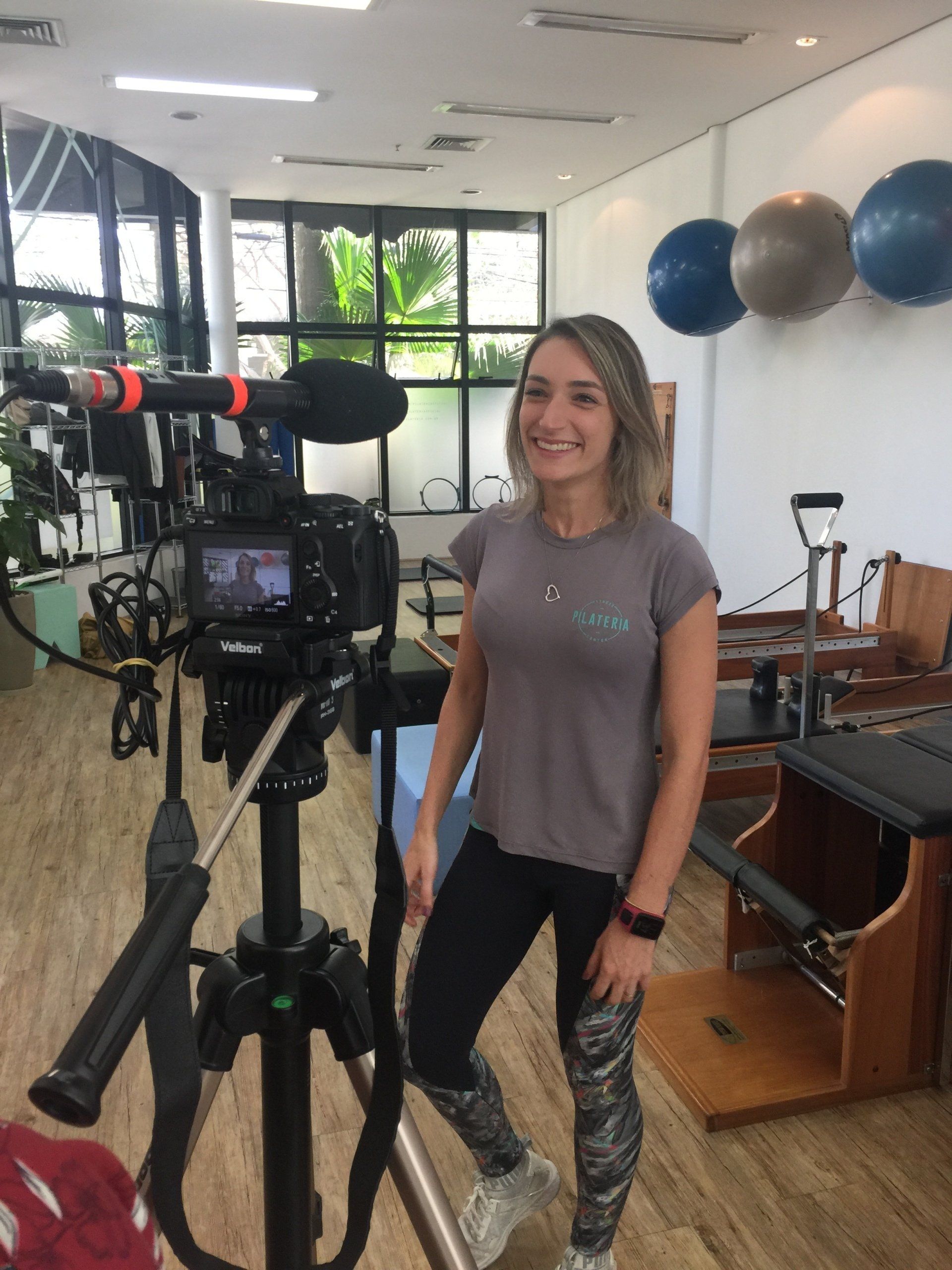 Uma mulher está diante de uma câmera em uma academia.