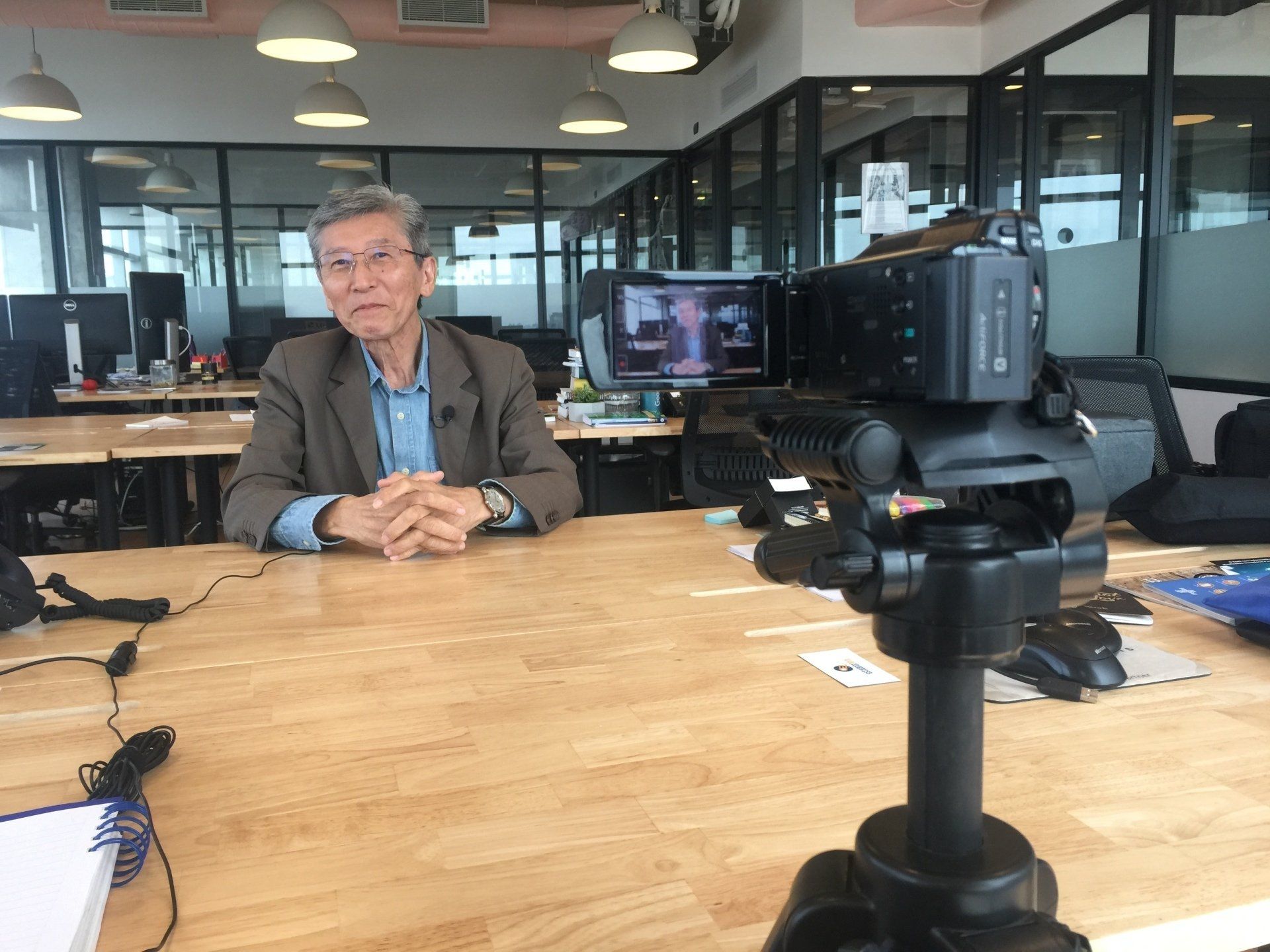 Um homem está sentado em uma mesa em frente a uma câmera.