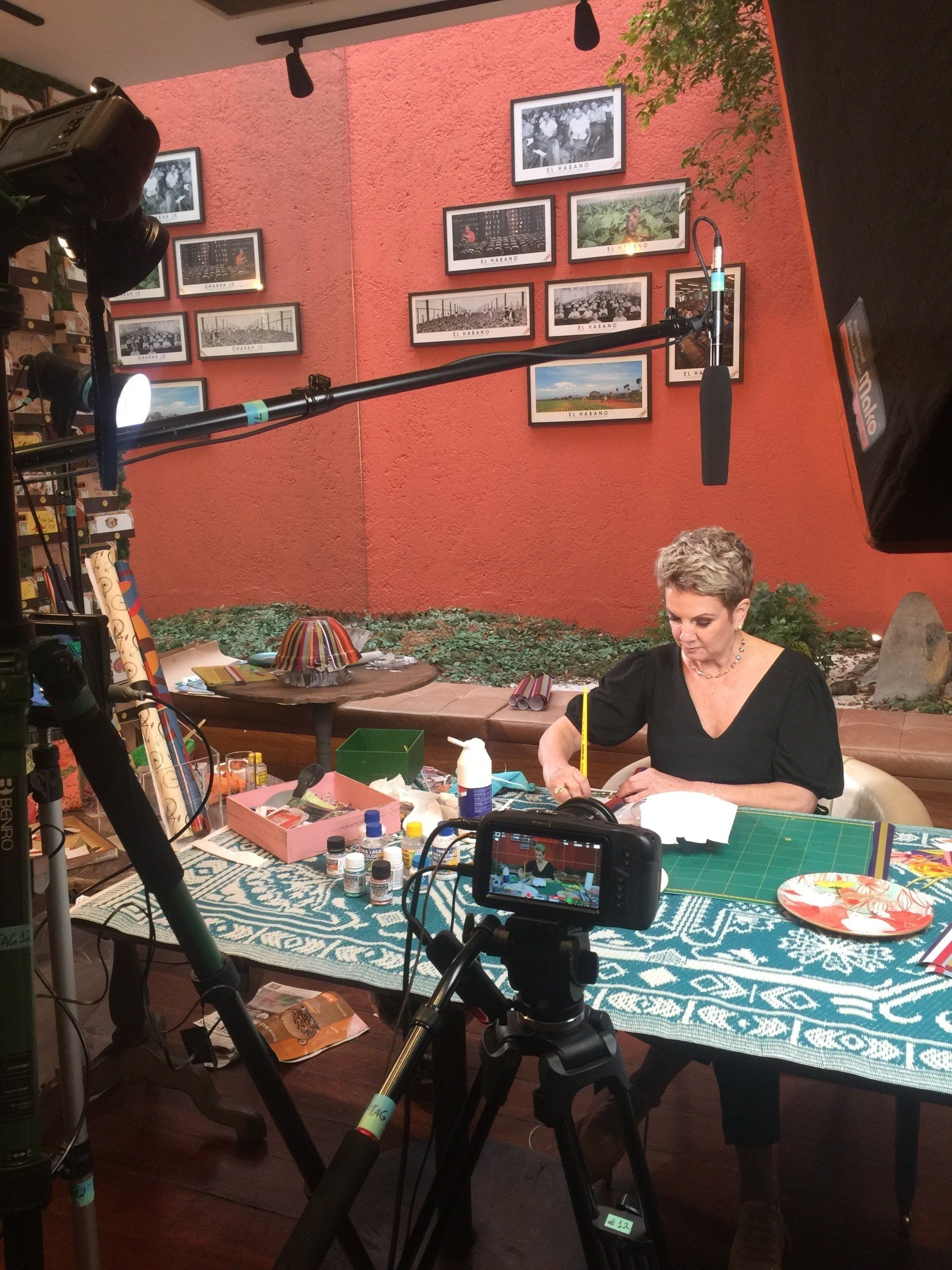 Uma mulher está sentada em uma mesa na frente de uma câmera