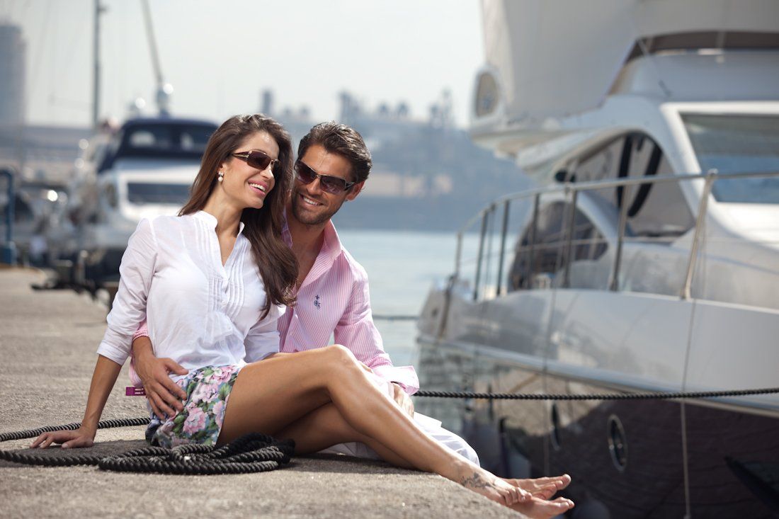 Um homem e uma mulher estão sentados em um cais ao lado de um barco.