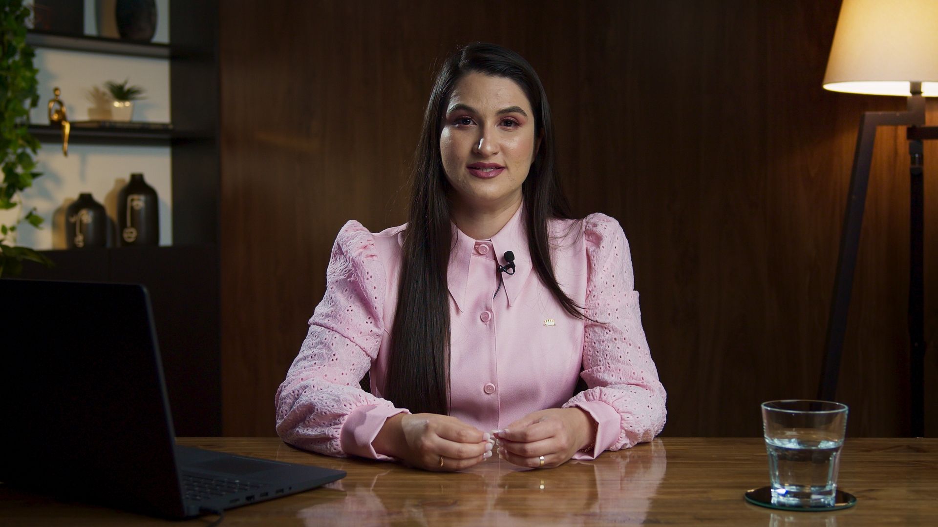 Uma mulher está sentada em uma mesa com um laptop e um copo de água.