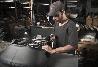 Um homem está trabalhando em um assento de motocicleta em uma fábrica