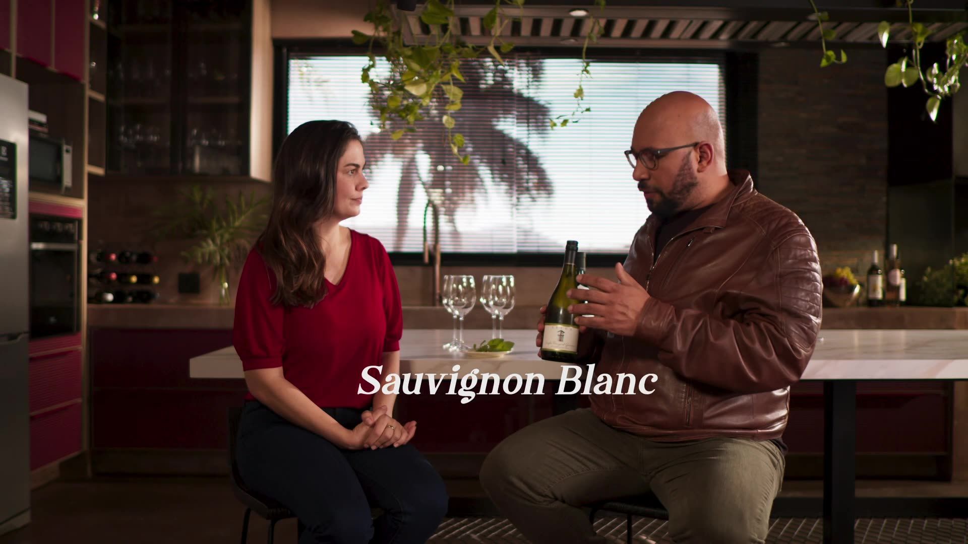 A man and a woman are sitting at a table with a bottle of sauvignon blanc.