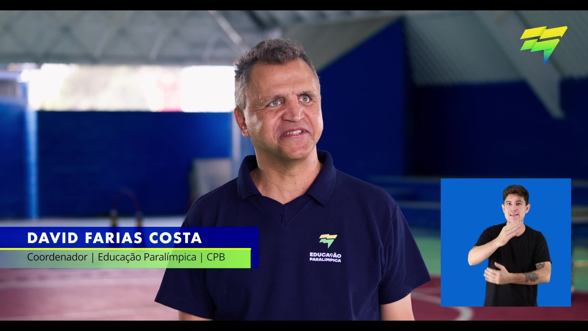 Um homem de camisa azul está parado em frente a uma placa de linguagem de sinais.