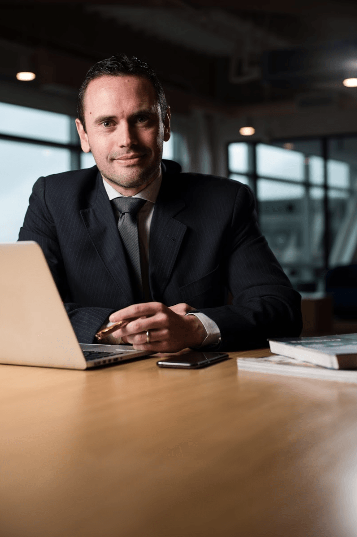 Um homem de terno e gravata está sentado à mesa com um laptop.