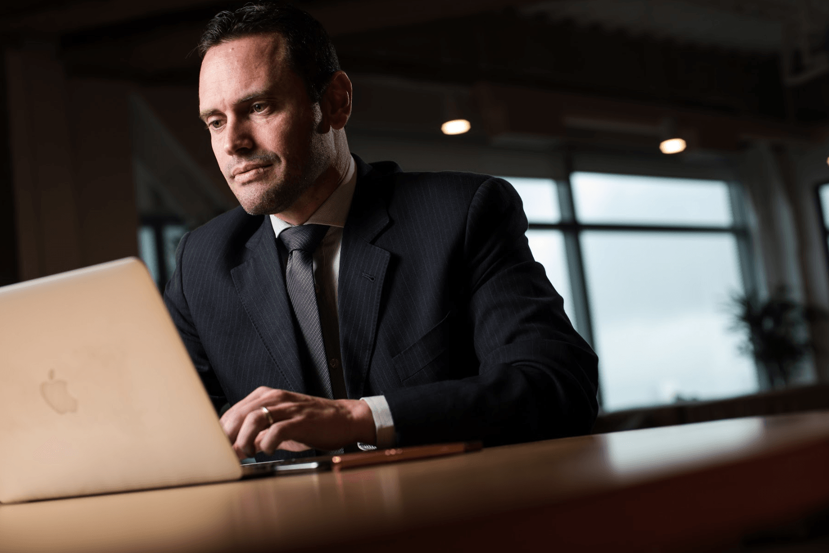 Um homem de terno e gravata está sentado a uma mesa usando um laptop.