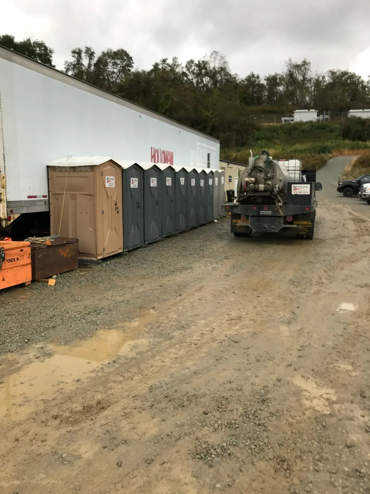 A truck is driving down a dirt road next to a row of portable toilets.