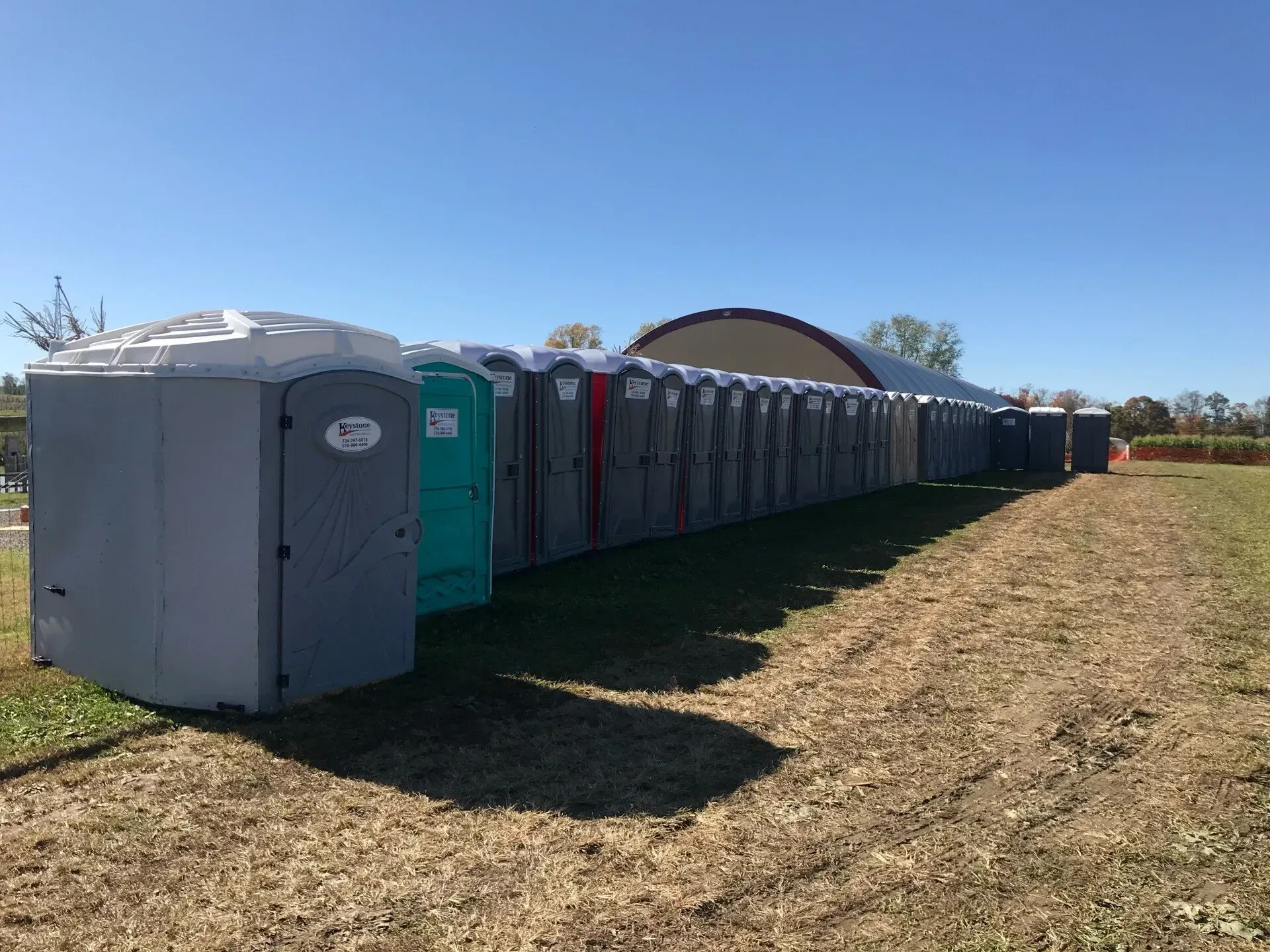 A row of portable toilets are lined up in a field.