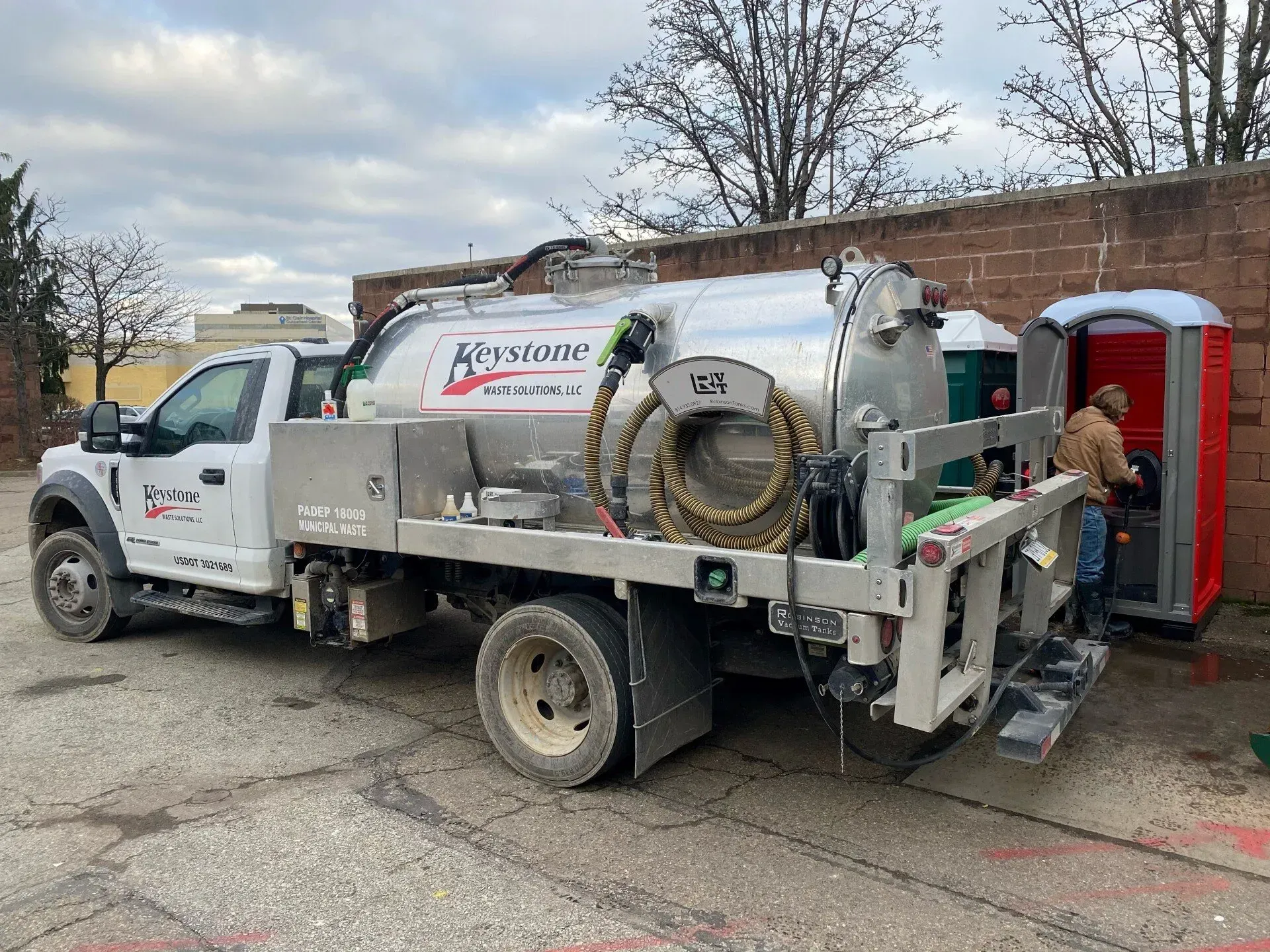 A vacuum truck is parked in front of a brick wall next to a portable toilet.