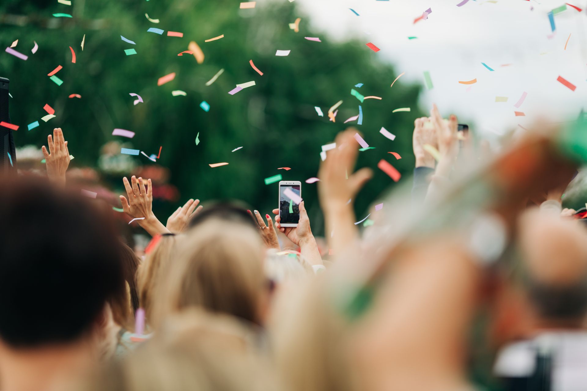 People with raised arms celebrating outdoors with confetti.
