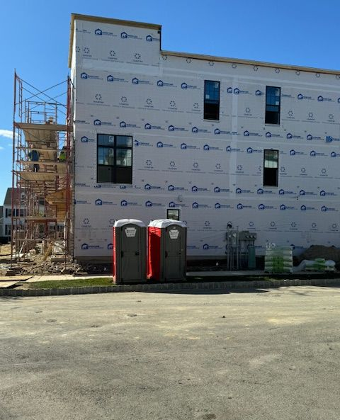 Two portable toilets on a construction site. A three-story building under construction, wrapped in white protective sheeting, with scaffolding and portable toilets.