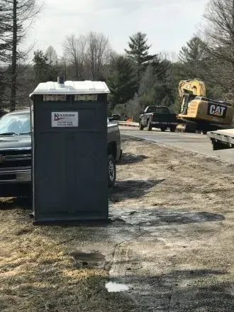A portable toilet is parked next to a truck in a dirt lot.