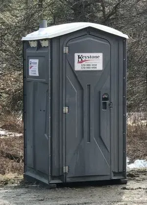 A portable toilet is sitting in the middle of a dirt field.