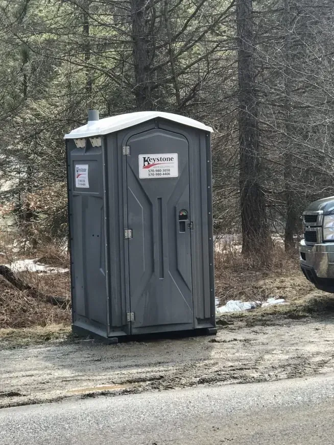 A portable toilet is parked on the side of the road next to a truck.