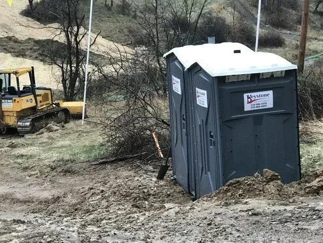 Two portable toilets are sitting in the dirt next to a bulldozer.