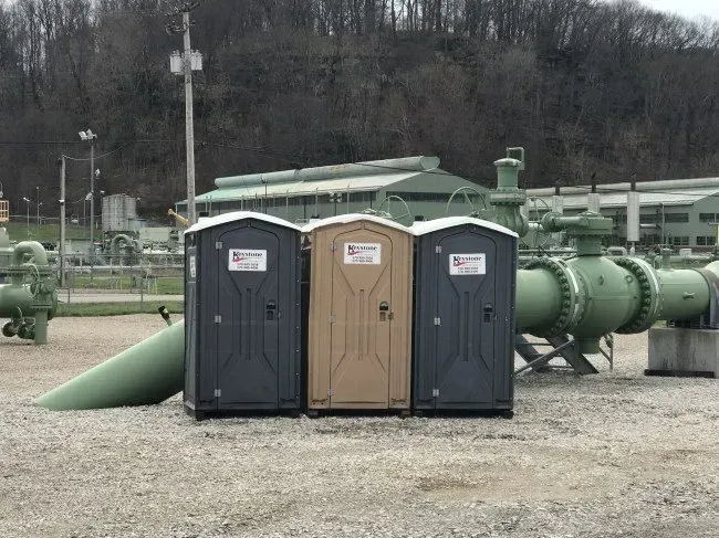Three portable toilets are sitting next to each other in a field.