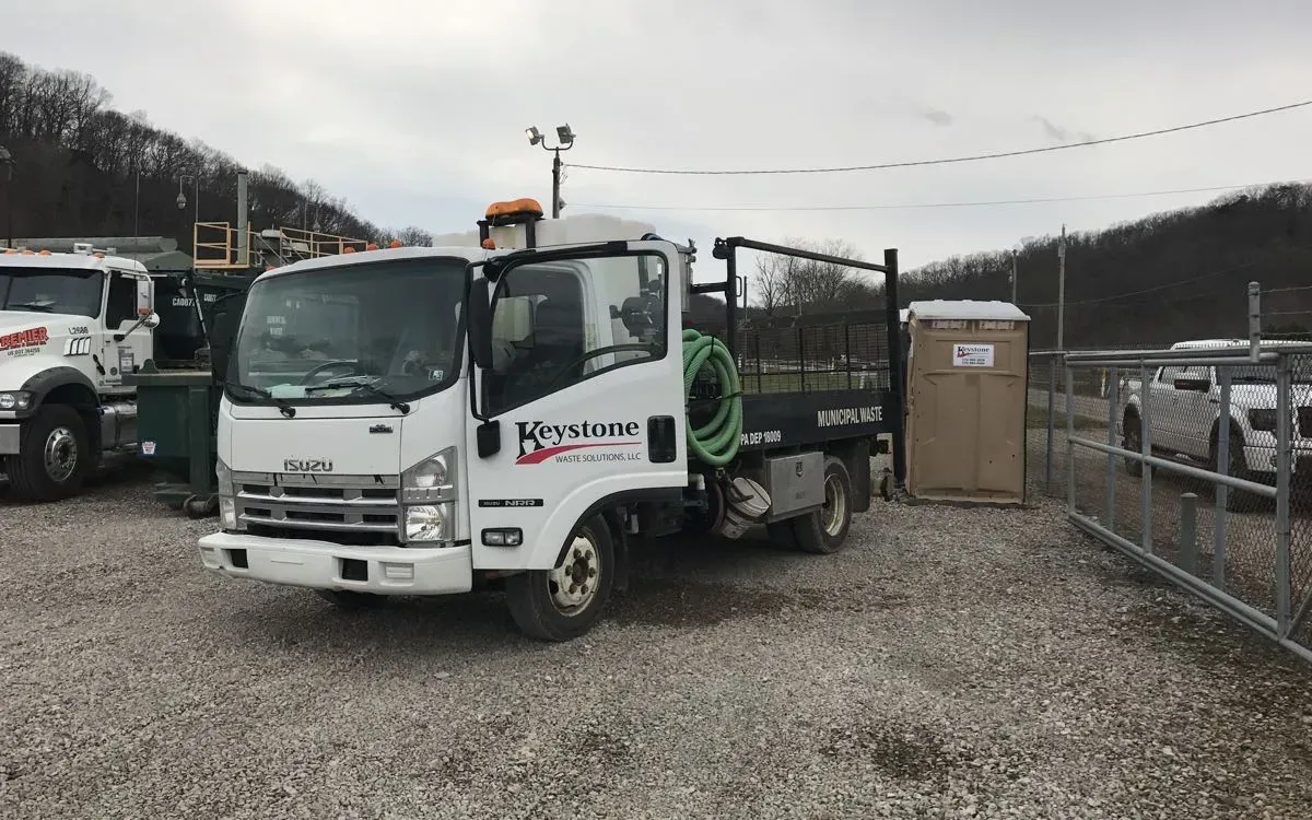 A white truck is parked in a gravel lot next to a fence.