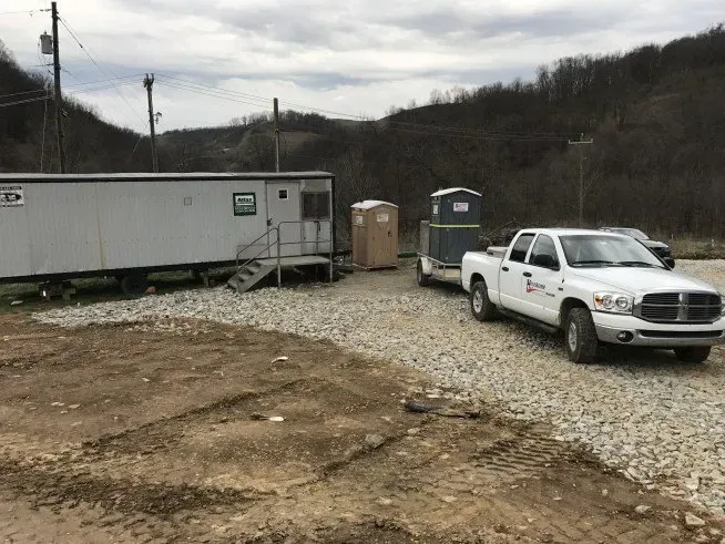 A white truck is parked in a gravel lot next to a trailer.