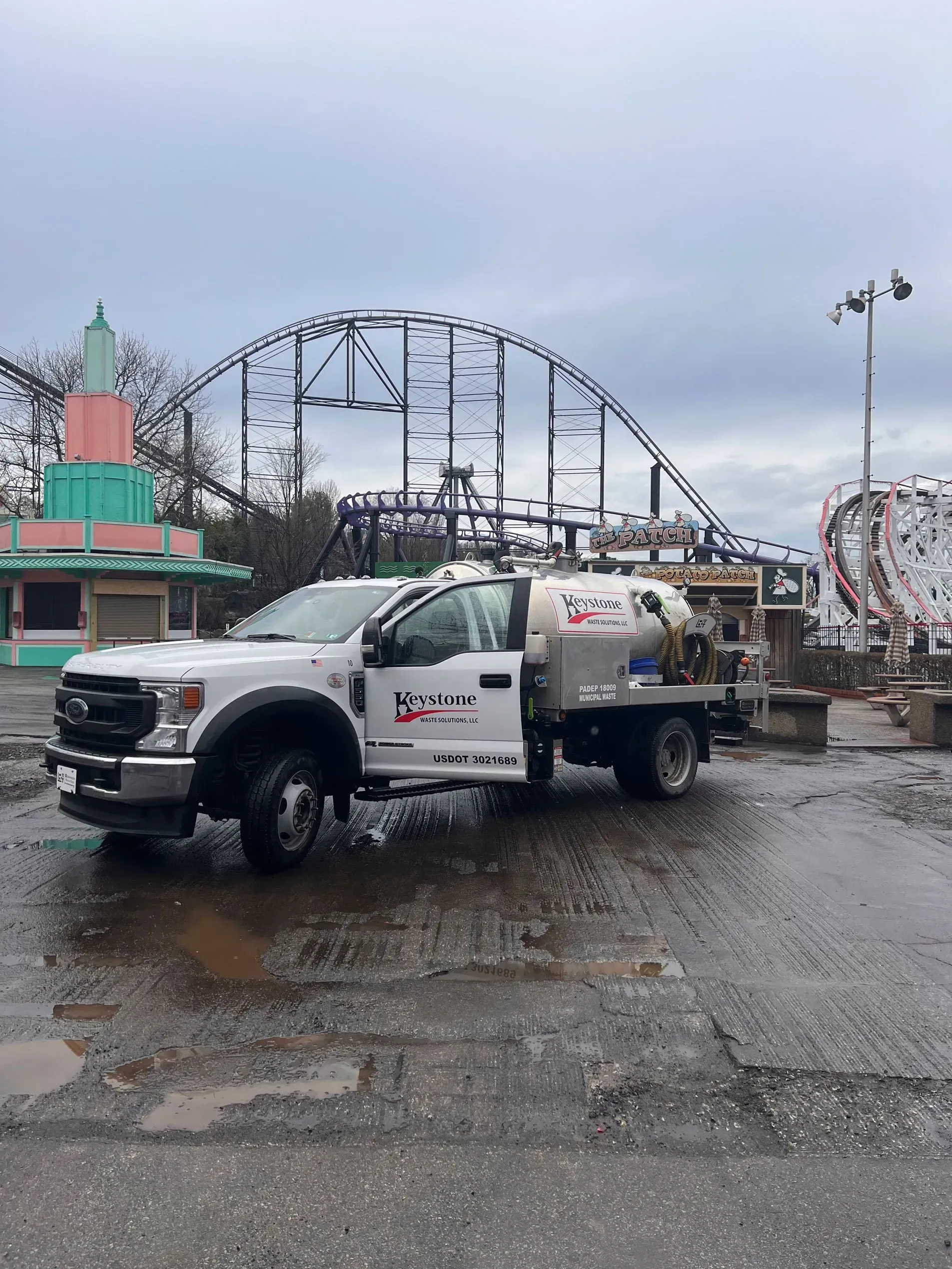 A white truck is parked in front of a roller coaster.