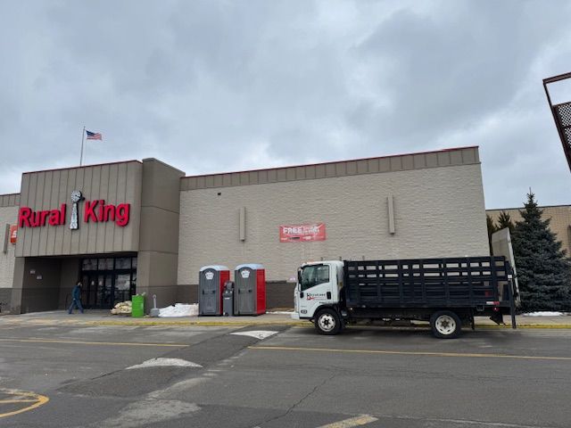 Rural King store with truck parked out front; porta-potties nearby. Grey sky and concrete lot.