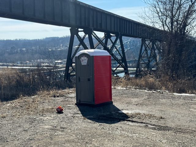Portable toilet near a bridge and river on a sunny day.