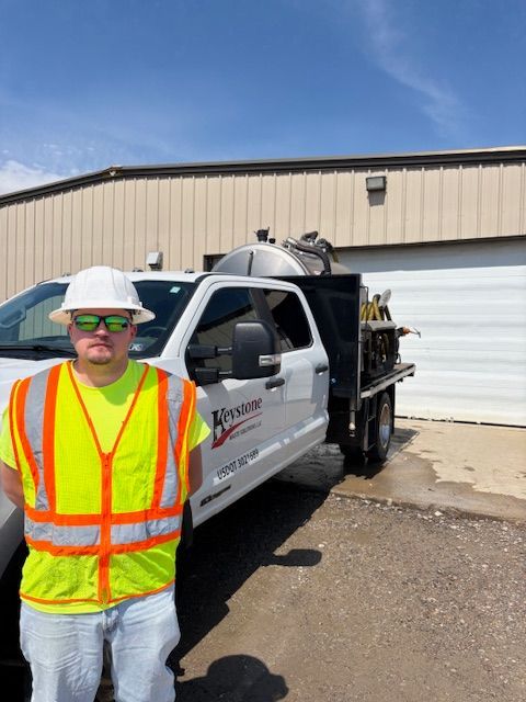 Worker in reflective vest and hard hat standing beside a utility truck outside a warehouse.