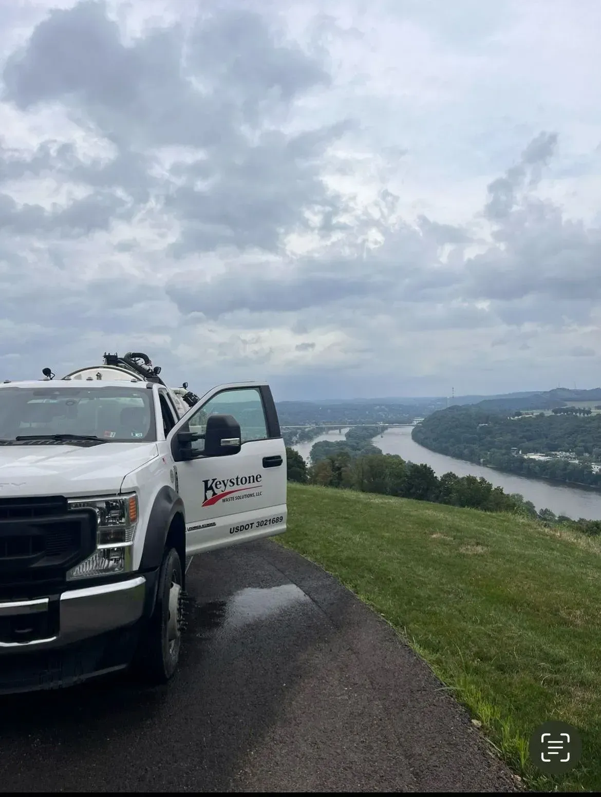 A white truck is parked on the side of a road overlooking a river.