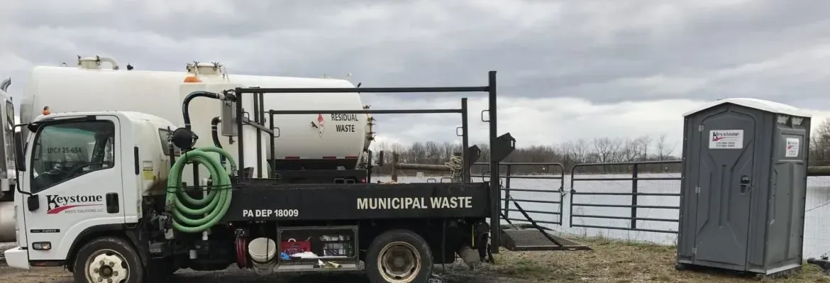A vacuum truck is parked next to a portable toilet.