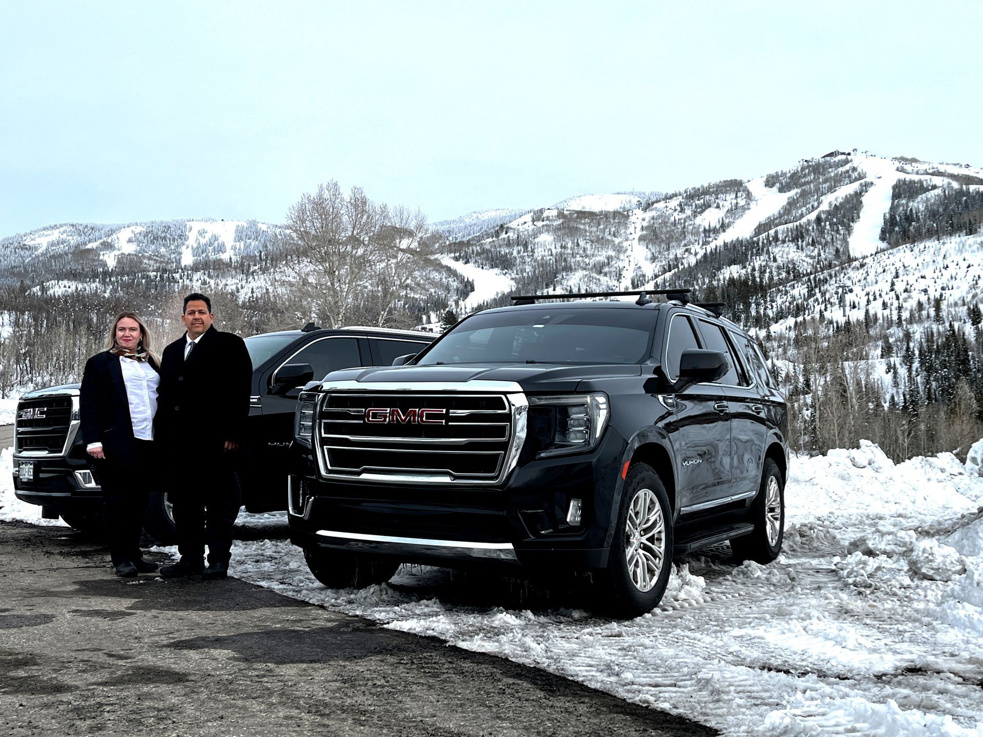 Two men are standing next to a gmc suv in the snow.