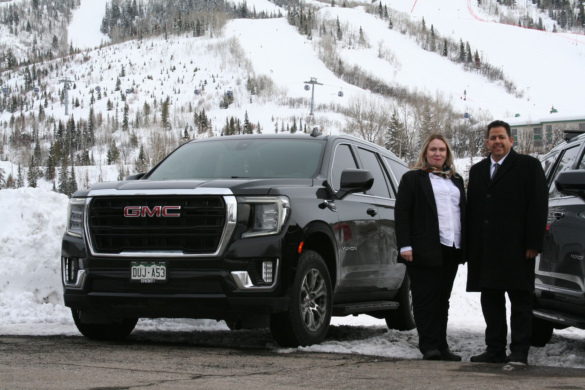 A man and a woman are standing in front of a gmc truck in the snow.