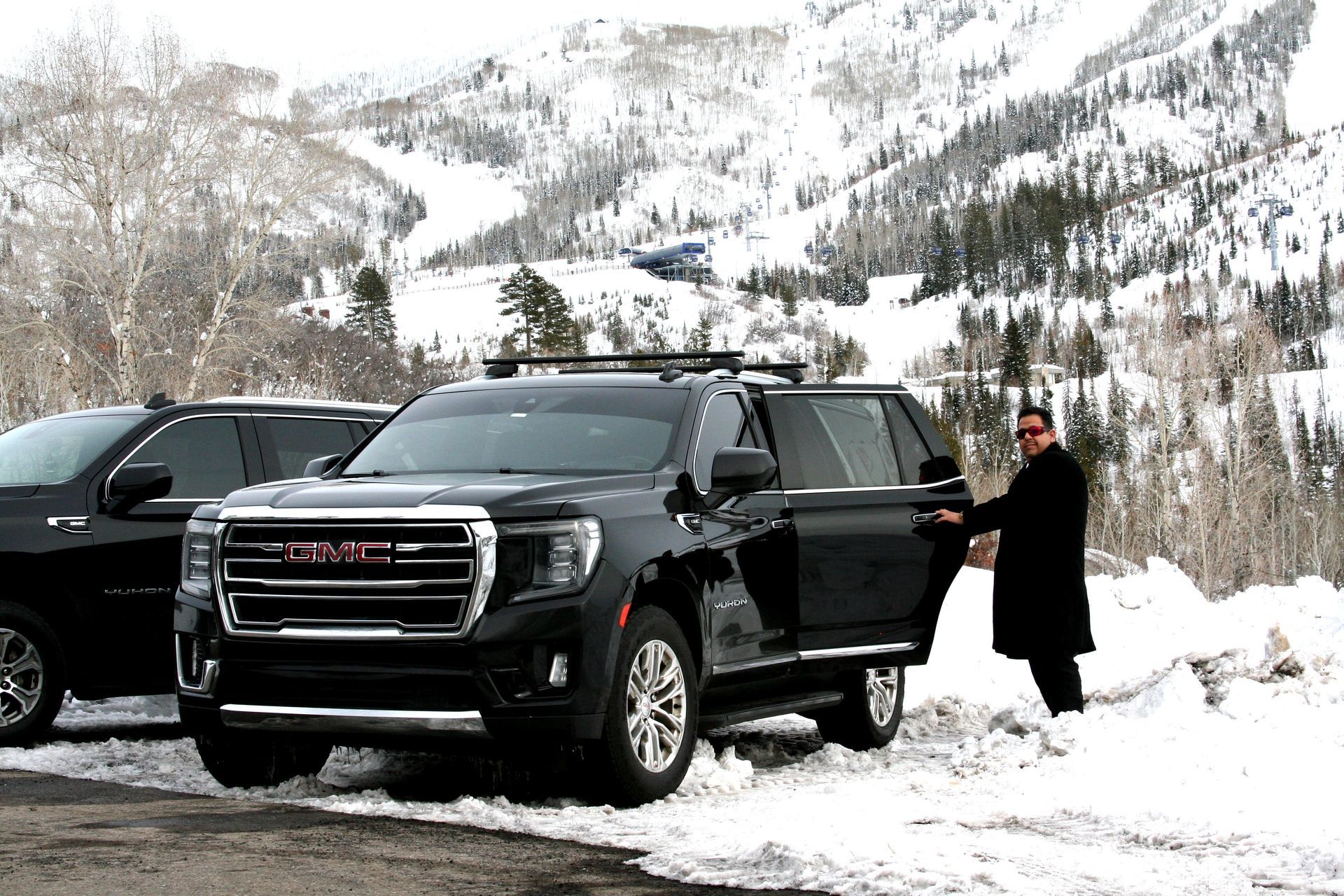 A man is opening the door of a gmc suv in the snow.