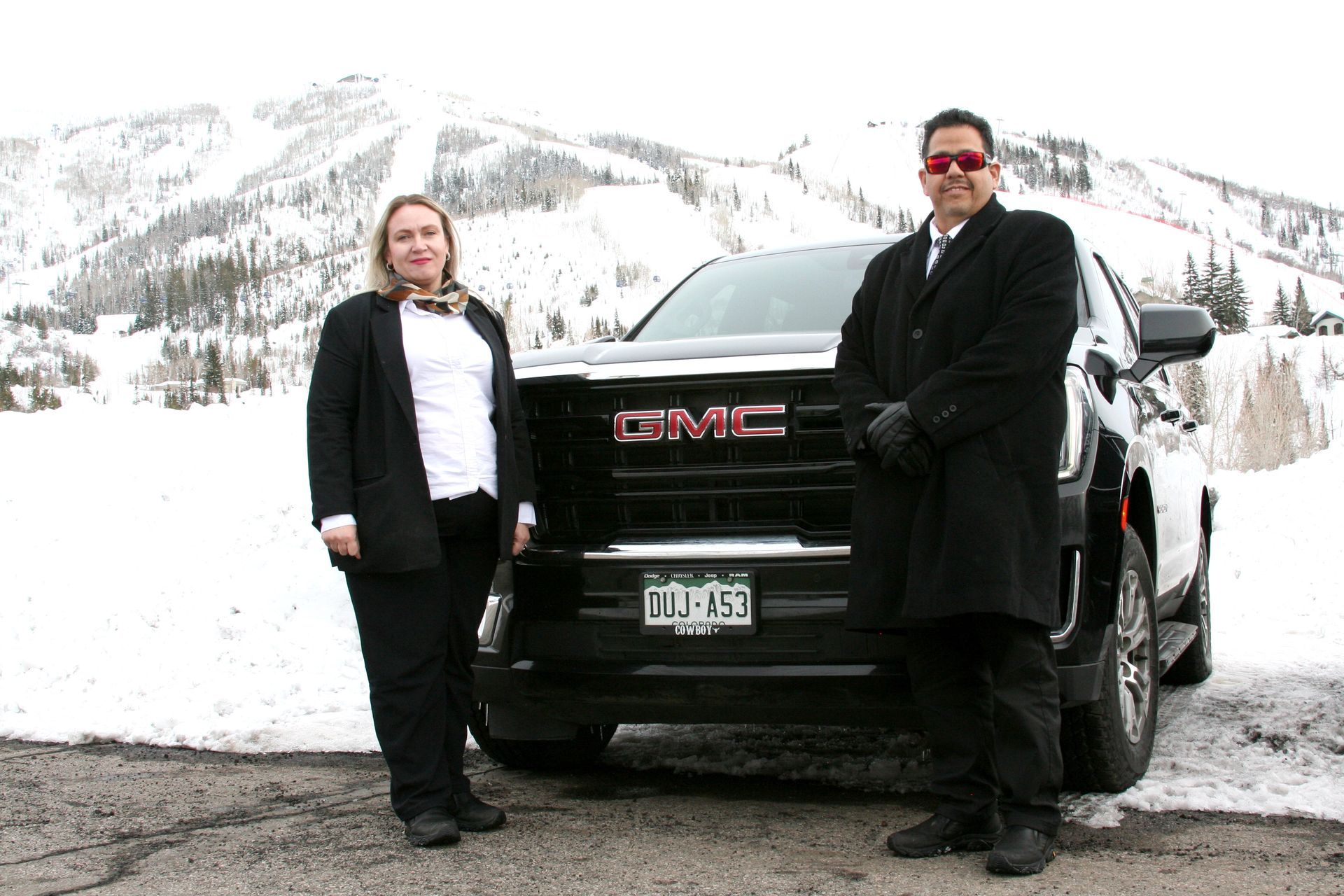 A man and a woman are standing in front of a gmc truck in the snow.