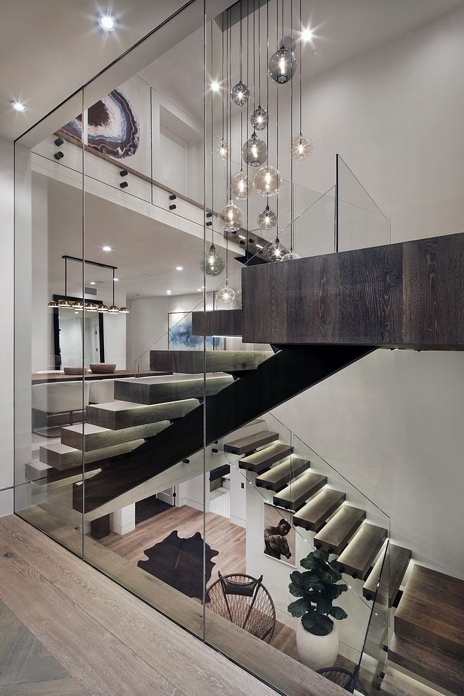 Modern staircase with glass walls, wooden steps, and a cascading light fixture.