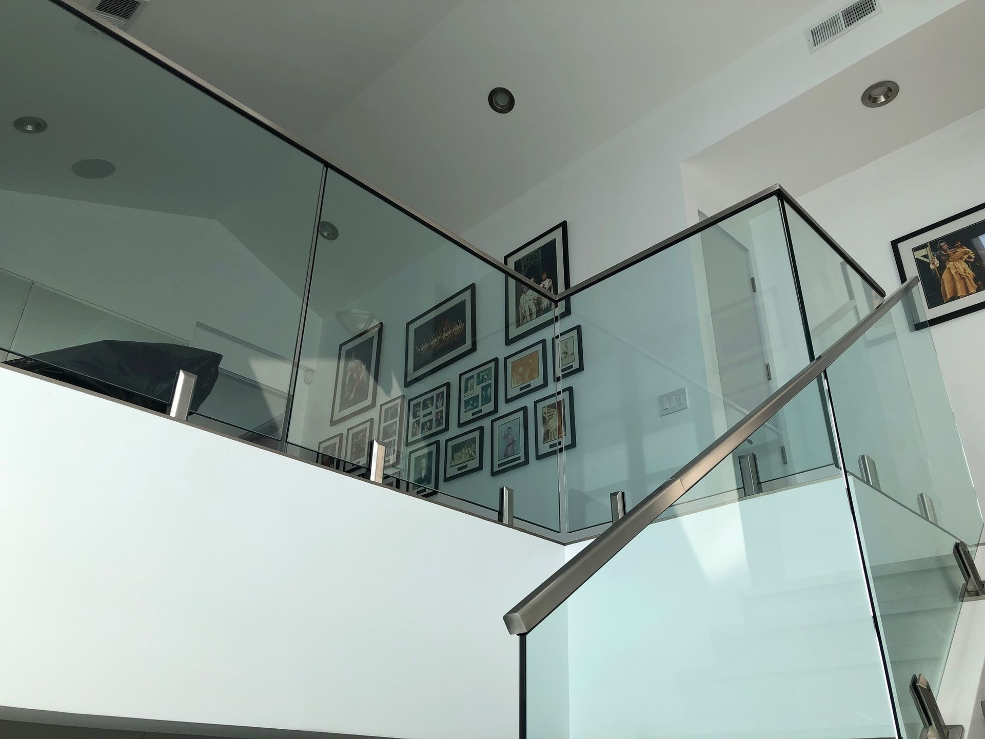 Glass railing with black trim and stainless steel posts alongside a staircase with art.