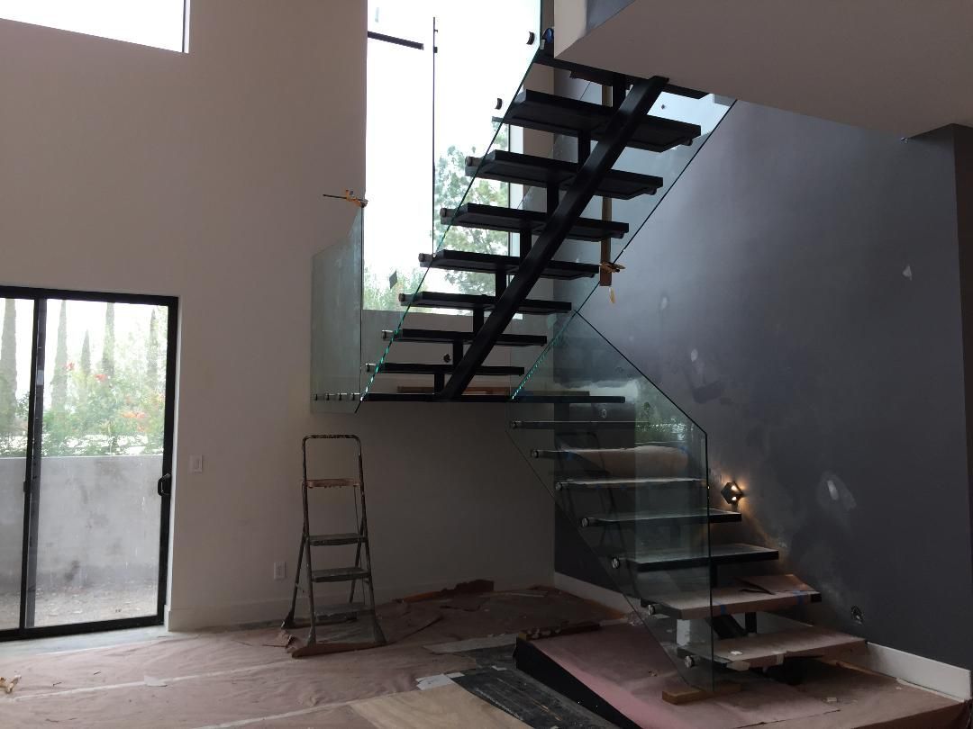 Modern interior with floating glass staircase and large windows.