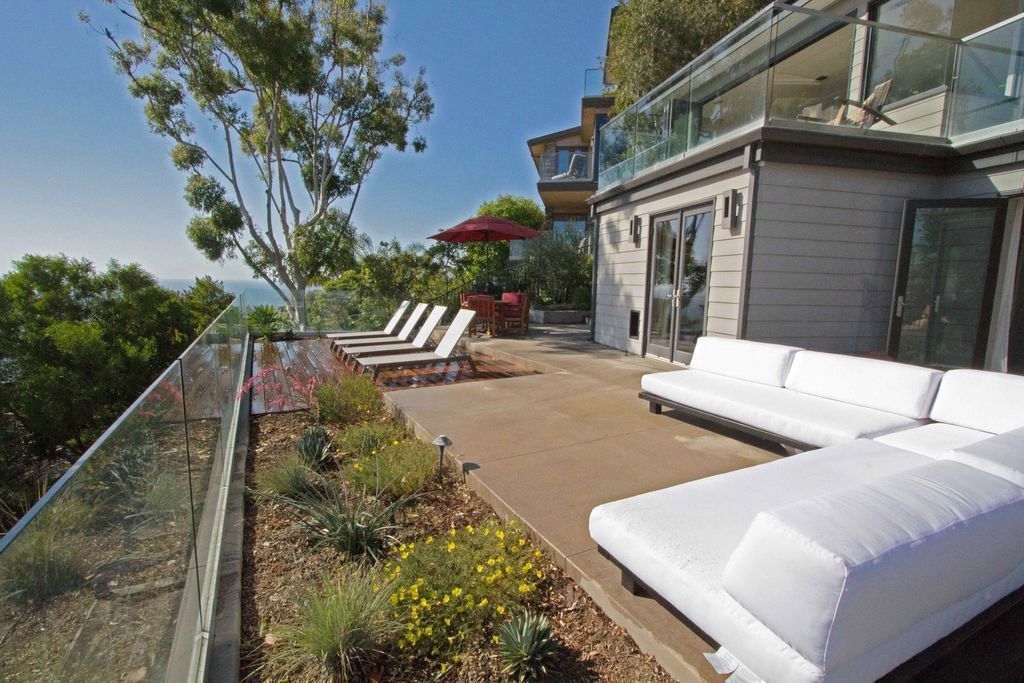 Patio with white couches, lounge chairs, and ocean view from a modern house.