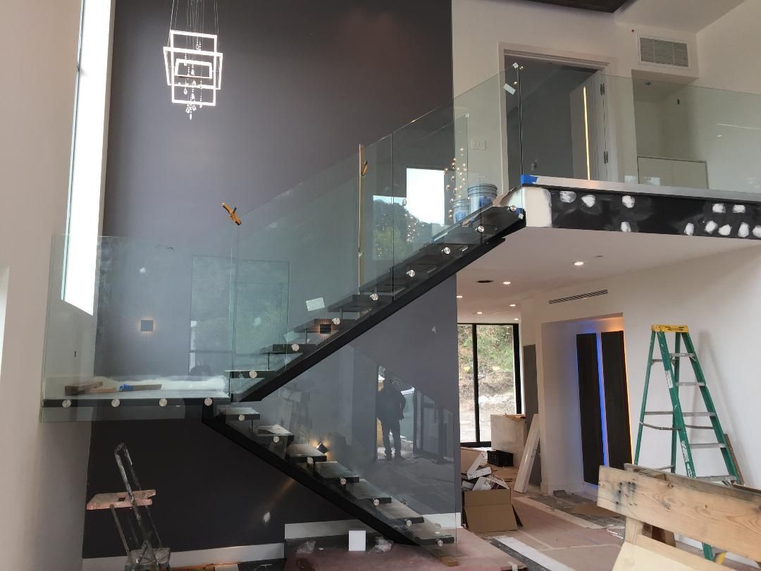 Modern staircase with glass railing and gray wall. Construction in progress.
