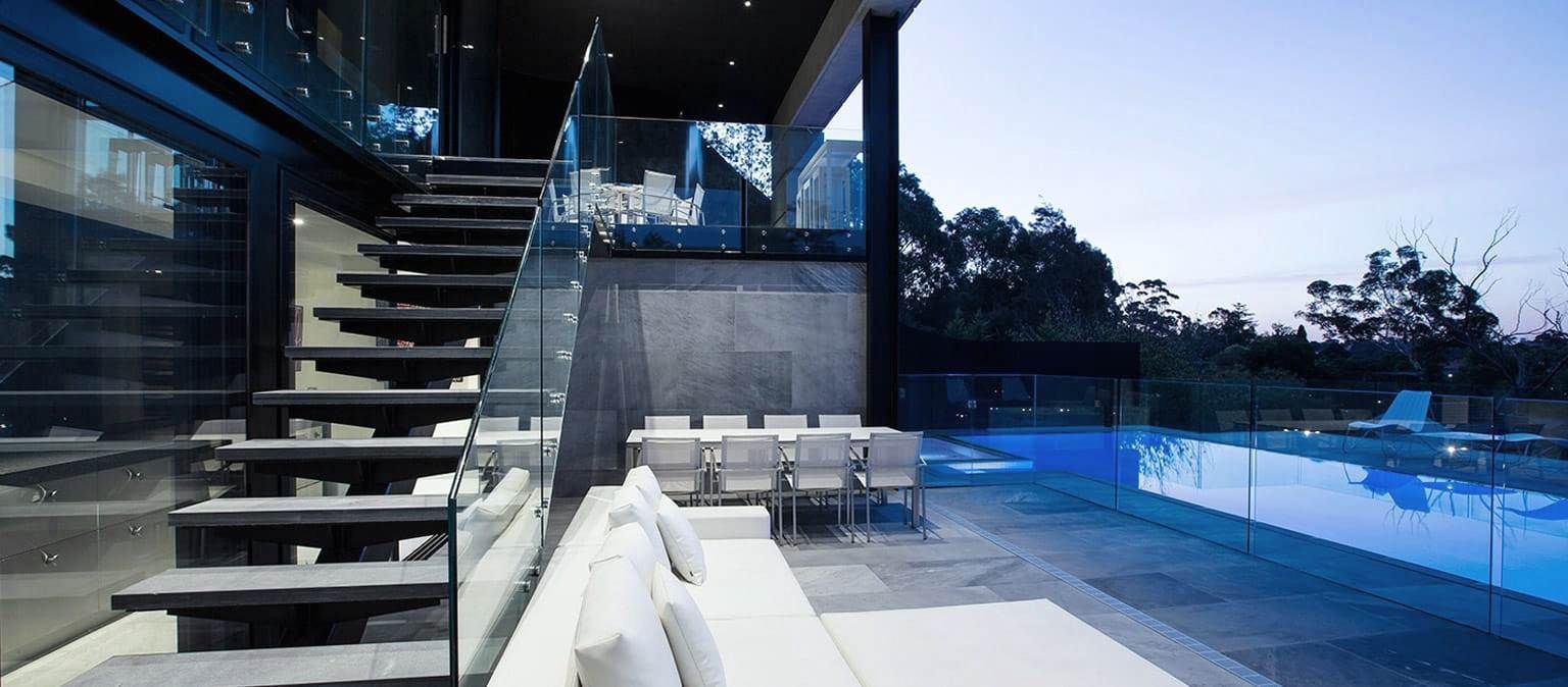 Modern home exterior with a staircase, pool, and outdoor dining area.