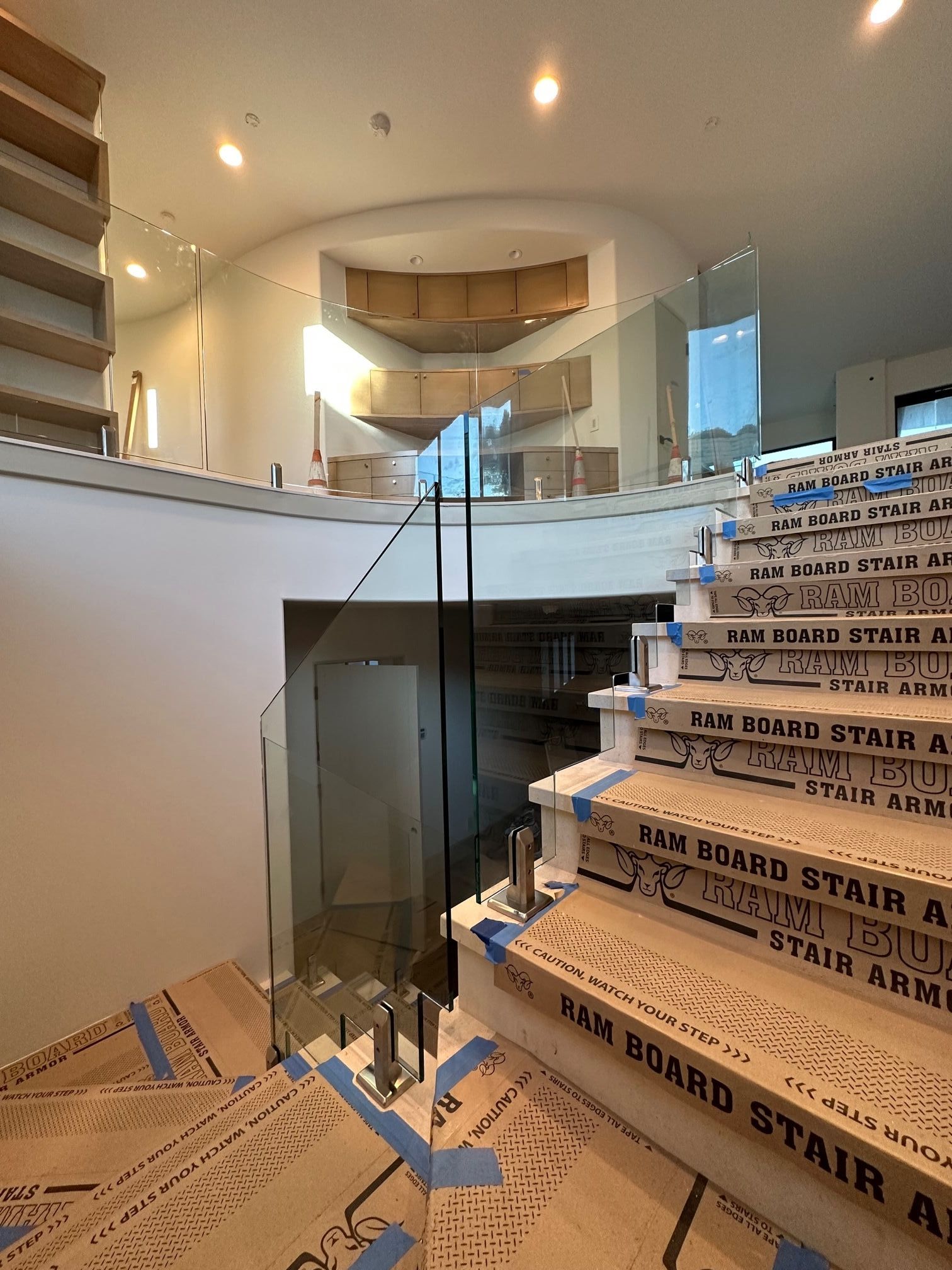 Curved staircase with glass railing. Cardboard covers protect steps. Light-filled interior with architectural details.
