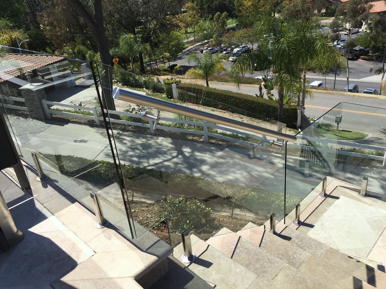 Glass railing on stone steps overlooking a road and trees in daylight.