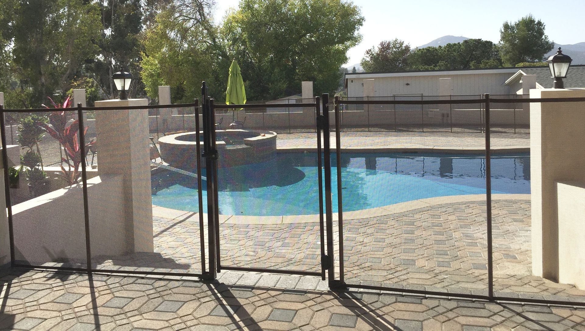 Black mesh pool safety fence surrounds a pool with stone patio.