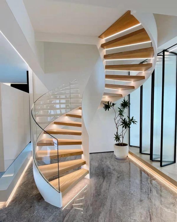 Spiral staircase with wood steps, glass railing, and white walls. A potted plant sits nearby.