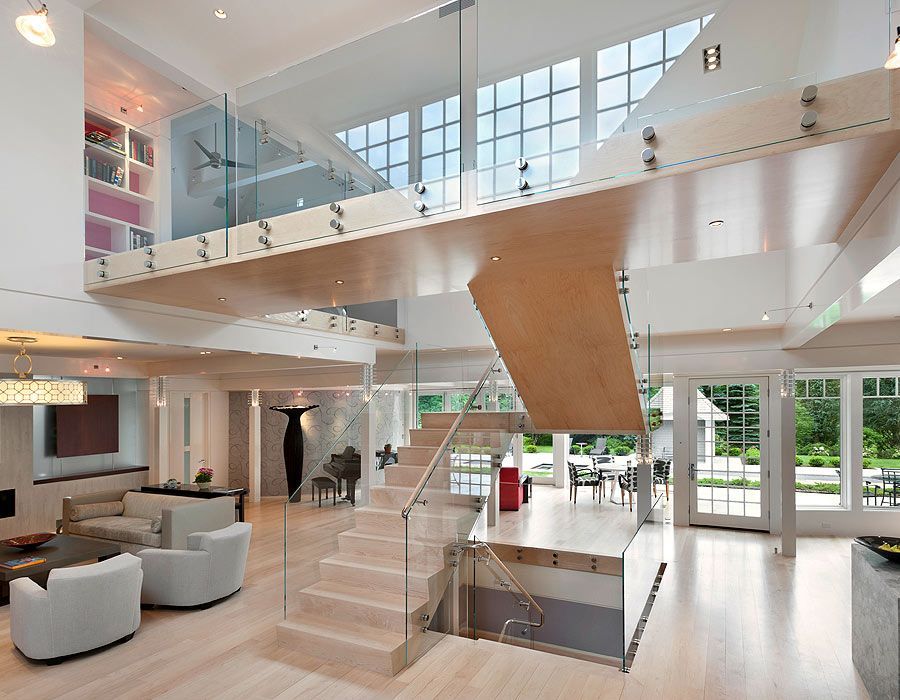 Spacious modern interior with a light wood mezzanine, glass railings, and stairs. Bright and airy living space.