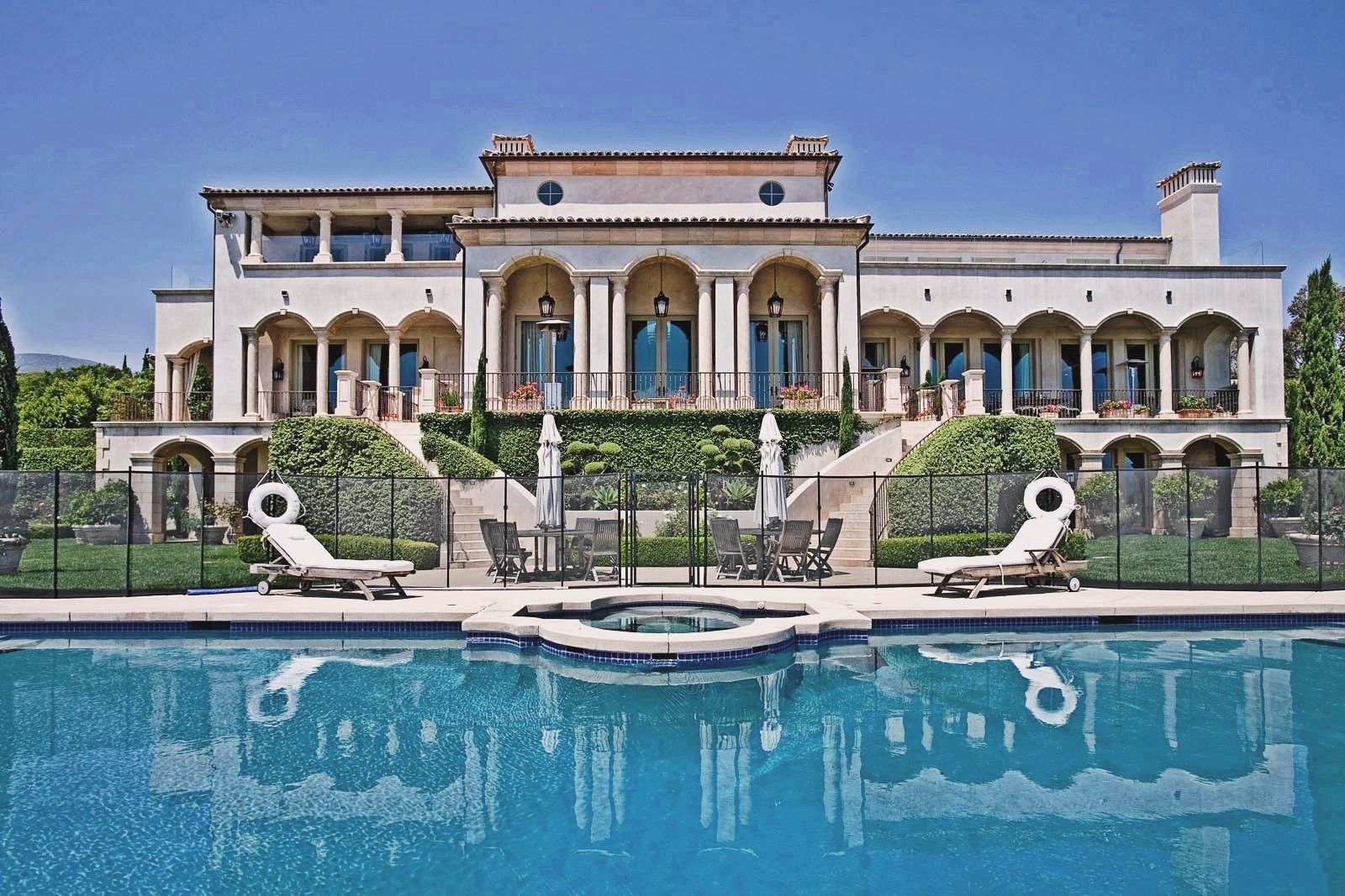 Luxurious mansion with pool, patio furniture, and reflecting water.